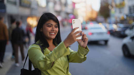 A beautiful multiracial young traveler is using her smart mobile phone to take photos and videos in the city.