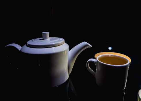 Restaurant, white teapot, white tea cup with tea, tea ceremony. Dark background