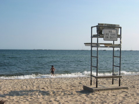 A boy running away from the waves on the beach - with a No Life Guard On Duty sign and station near by.More summer/beach photos: