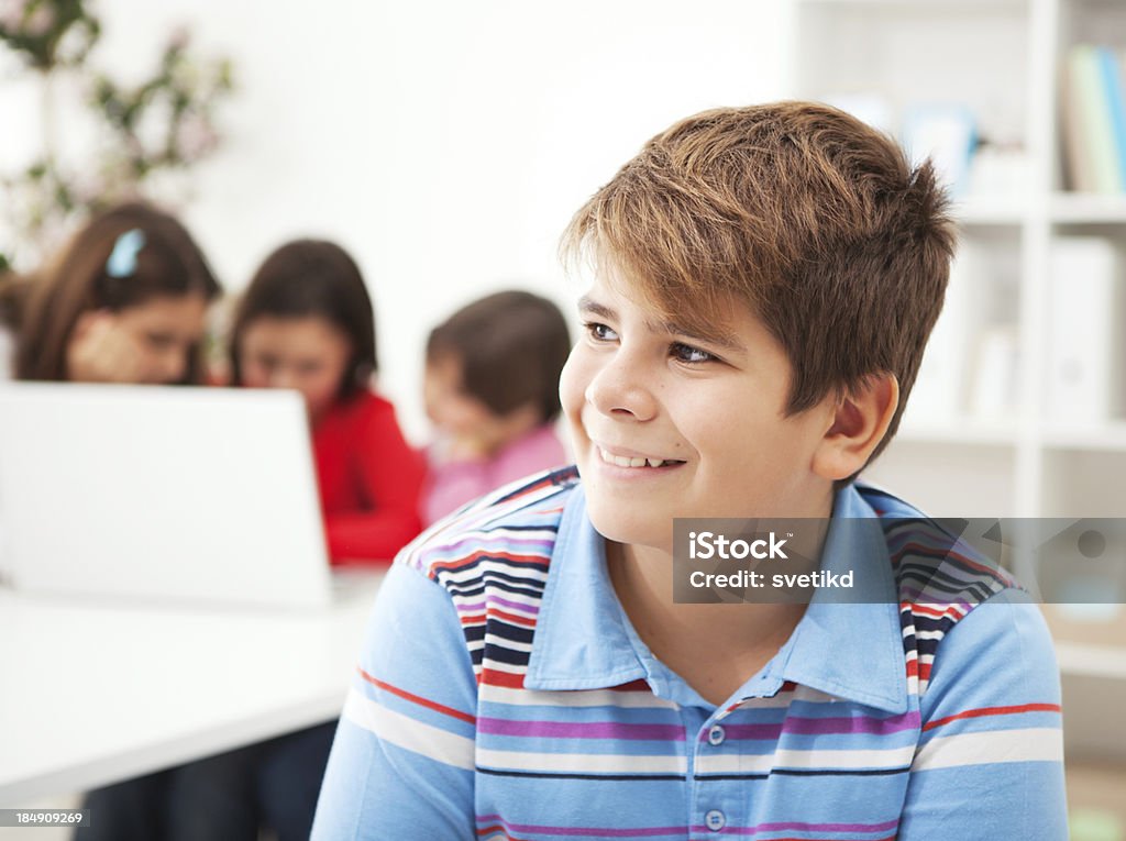 Smiling boy in classroom. Boy sitting and smiling in classroom with friends working on laptop in background. 12-13 Years Stock Photo