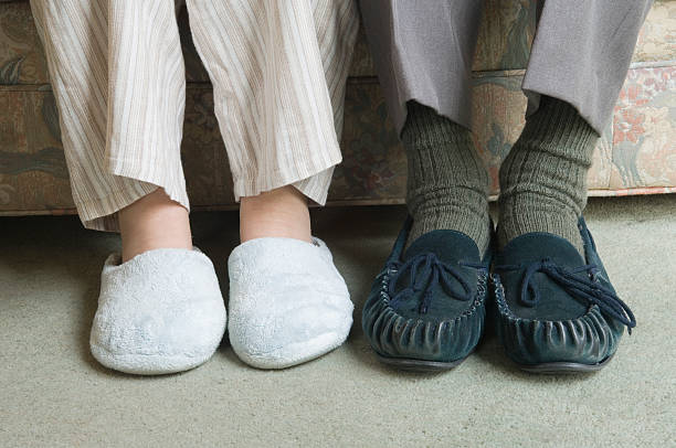 Two home slippers worn by people sitting on the couch stock photo