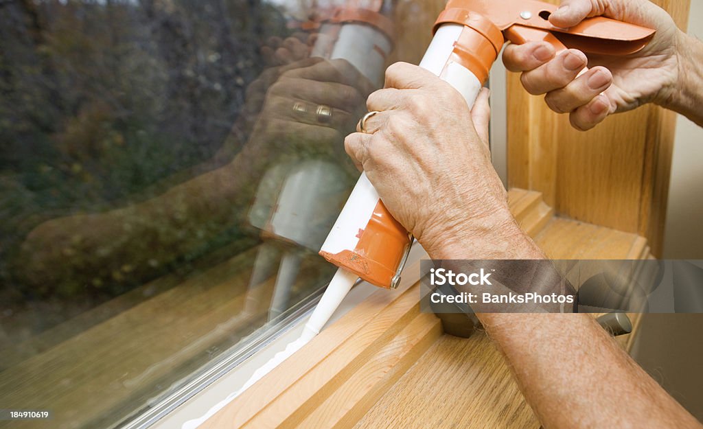 Hands Applying Weather Seal Caulk to Window Frame  Caulk Gun Stock Photo