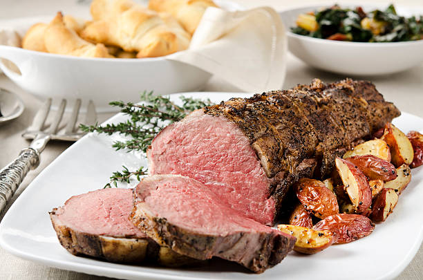 Roast Beef Tenderloin Dinner "SEVERAL MORE IN THIS SERIES. Prime beef tenderloin is barded with pork fat, tied, then cooked medium rare.  Roasted potatoes, crescent rolls, and sauteed chard accompany the roast beef.  Shallow DOF." roasted stock pictures, royalty-free photos & images