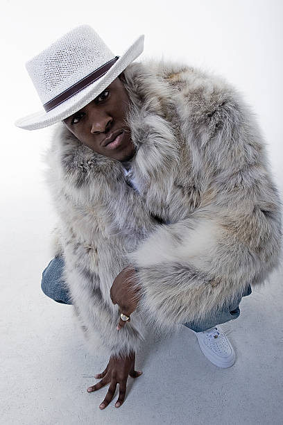 Up in Your Face Black man in fur coat leaning & crouching.* Studio floor and background are visible. pimp hat stock pictures, royalty-free photos & images