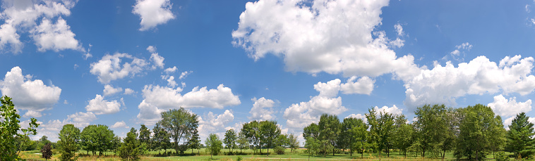 Lush green trees in park, with deep blue skies and fluffy white clouds in background. This is a large, high-resolution panorama created from several images stitched together.