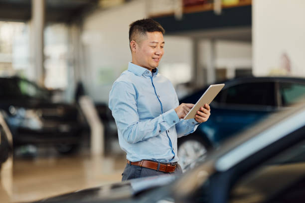 istock Happy Asian salesman using touchpad in a car showroom. 1849121871
