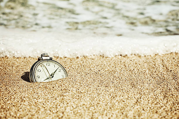 The Sands of Time "Photo of an old broken pocket watch half buried in the sand on a beach, being  washed away by the surf." broken pocket watch stock pictures, royalty-free photos & images