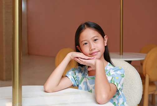 Beautiful Asian girl child age about 9 years old sit on chair and lying on marble table with looking camera.