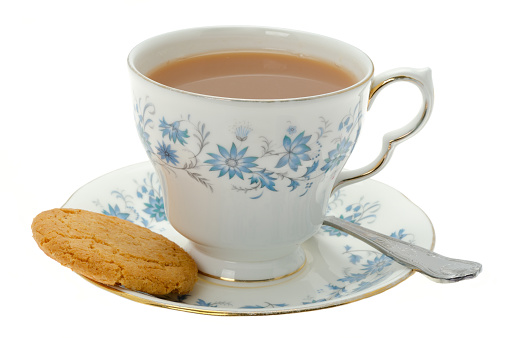 A cup of hot tea served in an ornate patterned cup and saucer with a cookie biscuit - studio shot.