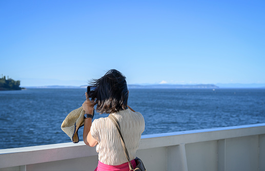 Woman taking photos using smartphone on the cruise ship on holiday. Washington State. USA.