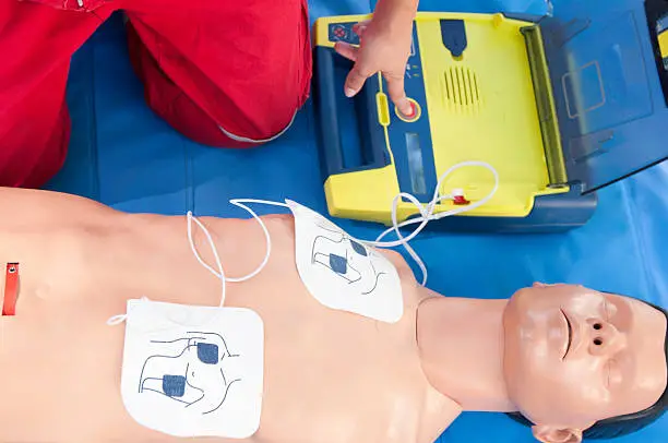 Paramedic activating portable defibrillator connected to CPR dummy during resuscitation training. Focus on CPR dummy