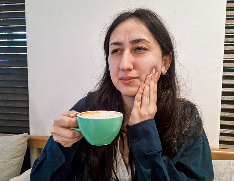 Young woman with sensitive teeth and hand holding glass of coffee with ice
