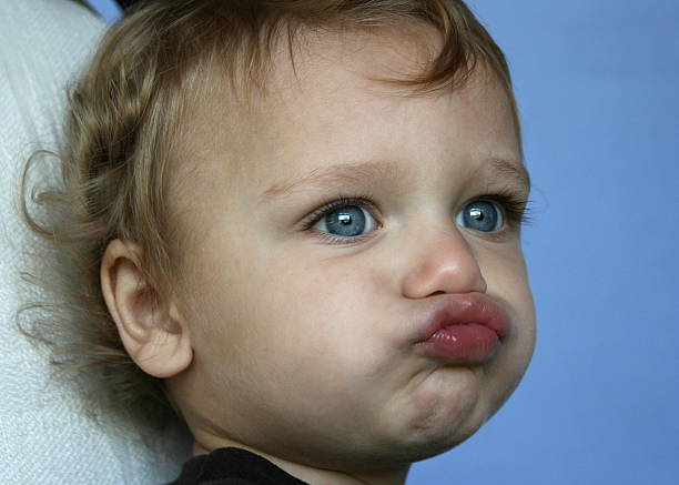 Ornery Boy Little boy with blue eyes making funny face on blue background.  To see more of this model: fish lips stock pictures, royalty-free photos & images