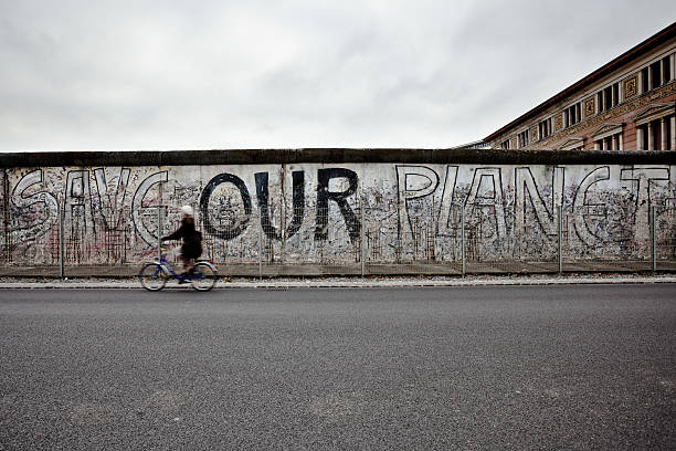 donna in bicicletta nella parte anteriore del muro di berlino, lato est, germania - east germany berlin germany graffiti wall foto e immagini stock