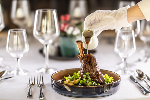 The chef or waiter finishes the meal right on the restaurant table, pouring the sauce over the leg of lamb confit.