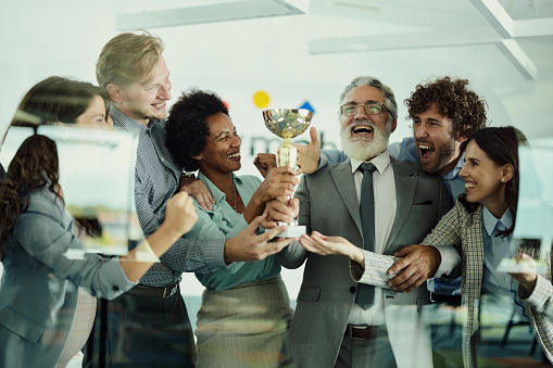 Group of cheerful entrepreneurs having fun while celebrating a trophy in the office. The view is through glass.