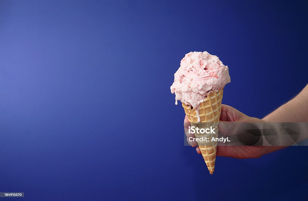 Strawberry Ice Cream Cone on Blue with Space for Copy A hand holding an ice cream cone. Ice Cream Stock Photo