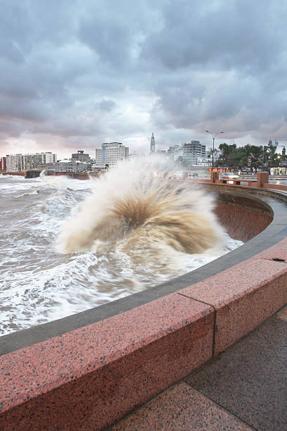 Waves crashing against the promenade with cityscape at background stock photo