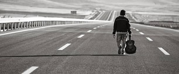 istock Young musician holding guitar and walking alone in highway 184915792