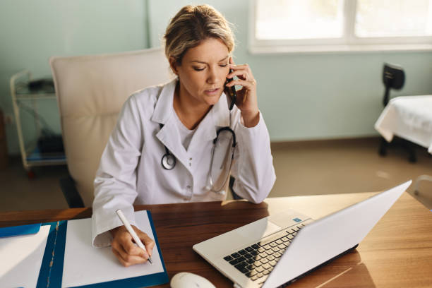 istock Female doctor talking on cell phone while working on laptop in the office. 1849165561