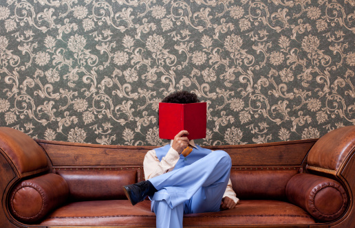 Young man in 1970s style reading book on sofa