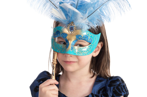 Horizontal studio shot on white of 6 year old girl with sly smile and mardi gras style mask.