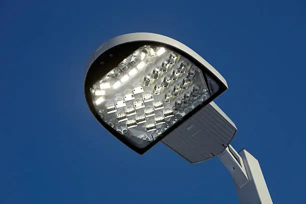 "A new, illuminated, LED streetlight against a clear blue sky at dusk. LEDs represent the latest in lighting technology, although initially more expensive than traditional lights, LEDs are being considered for energy efficient installations around the world. This particular light has the LEDs installed in directional modules which controls the light, eliminating glare and hot spots."