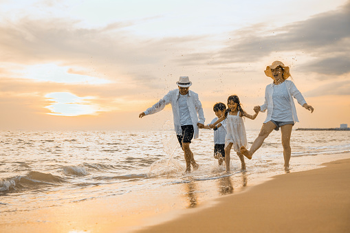People of father, mother, children son and daughter family of four holding hands together walking outdoor, Happy family having fun running on a sandy beach at sunset, tropical summer travel vacations