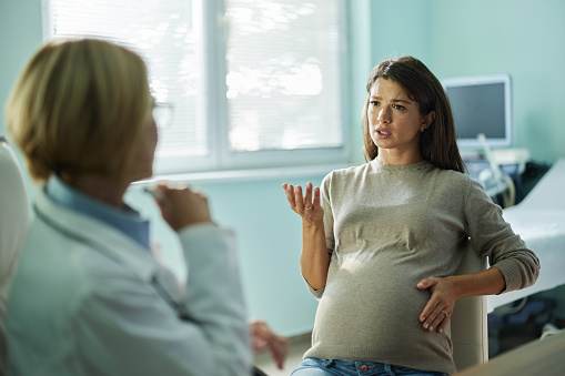 Pregnant woman communicating with her female gynecologist during a visit in the office.