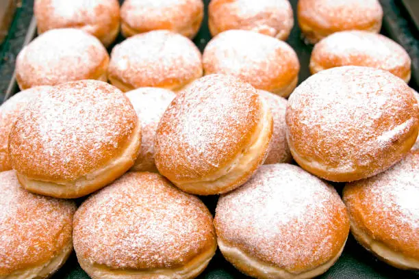 "Fresh baked German Jelly Doughnuts filled with strawberry jam or raspberry jam and dusted with powdered sugar. Full tray in a bakery counter display, delicious. Selective focus in foreground."