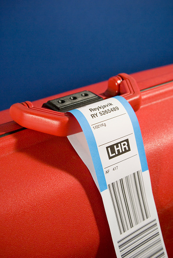 Red plastic suitcase on a blue background with reykjavik luggage label on the handle