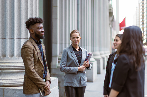 Business people talking outdoors. They are standing in front office building in Wall Street, Manhattan