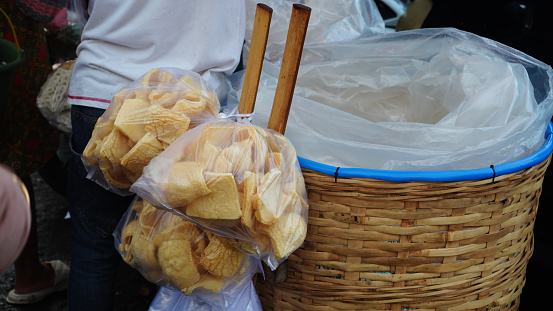 crackers in a white plastic bag hanging from a stick were next to a woven bamboo basket.