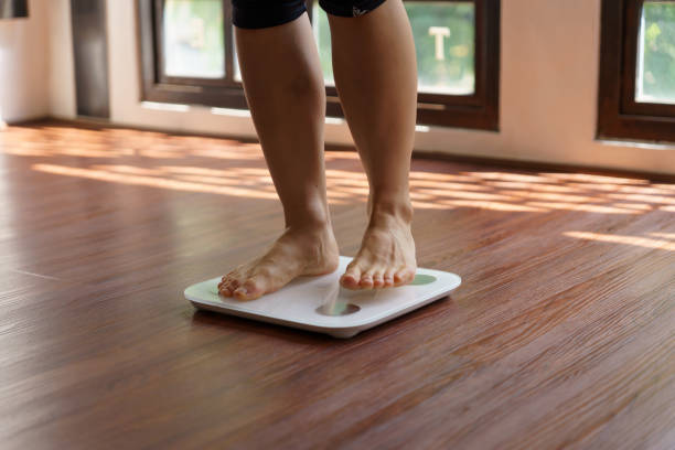 istock Fat diet and scale feet standing on electronic scales for weight control. Measurement instrument in kilogram for a diet control 1849201687