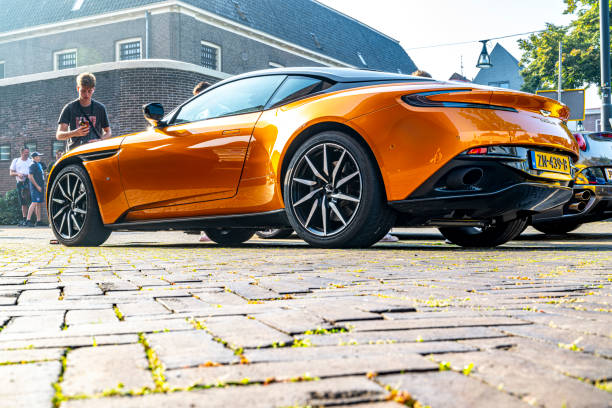 Aston Martin DB11 sports car in bright orange in the streets of Zwolle with people looking at the car. The Aston Martin DB11 is a luxury grand tourer unveiled in 2016 and available with V8 and V12 petrol engines.