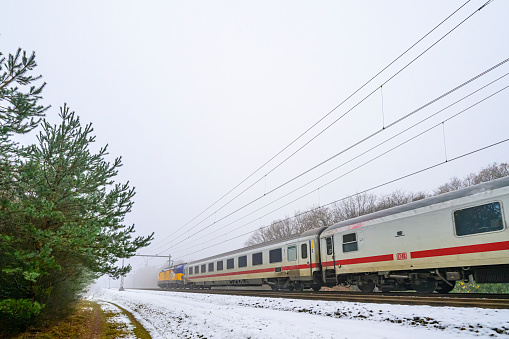 International train of the Dutch Railways driving through the snow on a cold day in the Veluwe nature reserve in winter.