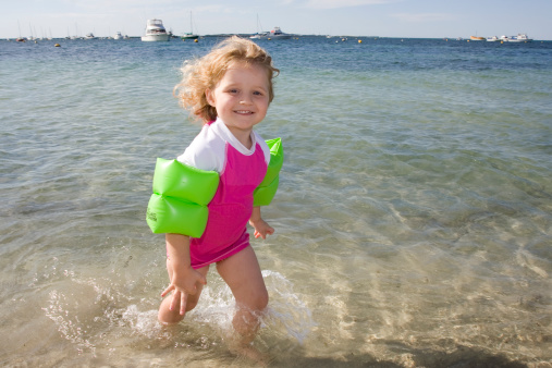 A little girl wearing floaties at beach.