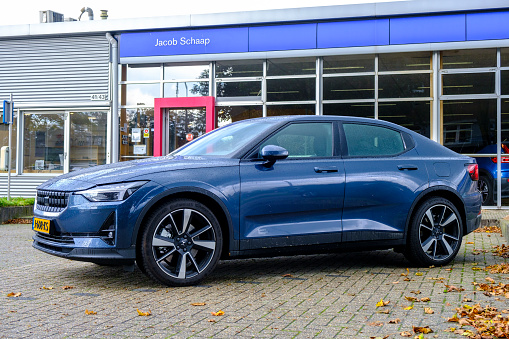 Polestar 2 all-electric 5-door fastback car in blue parked in front of a Volvo dealership.  Polestar is the performance company and brand of Volvo Cars now focussed on producing electric and hybrid vehicles. The Polestar 2 is powered by two electric motors driving the front and rear wheels.