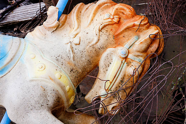 A broken child's toy riding horse in a junk yard. Covered with rusted wire and garbage.
