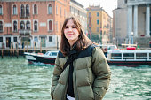 Portrait of beautiful teenage girl standing by Grand Canal and smiling at camera, visiting Venice, Italy