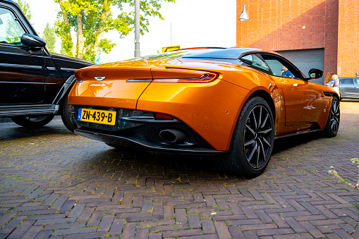 Aston Martin DB11 sports car in bright orange in the streets of Zwolle with people looking at the car. The Aston Martin DB11 is a luxury grand tourer unveiled in 2016 and available with V8 and V12 petrol engines.