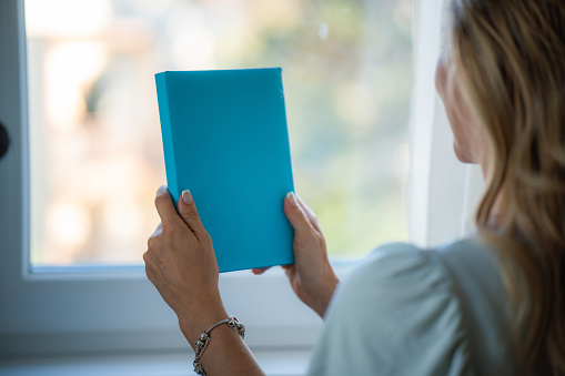 Close-up of a woman holding a book against window at home