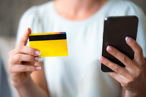 Close-up of unrecognizable woman holding credit card providing payment using phone app
