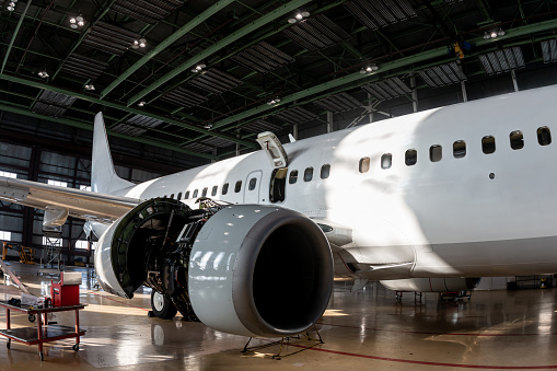 White passenger airliner in the aviation hangar. Aircraft under maintenance. Checking mechanical systems for flight operations