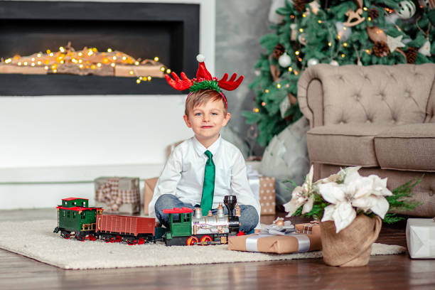 buongiorno. bambino felice con un regalo, treno giocattolo, sotto l'albero di natale la mattina di capodanno. è ora di soddisfare i desideri. - mago national park foto e immagini stock