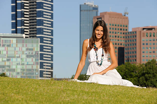 Beautiful woman sitting in the grass with the skyline of Melbourne in back. Nikon D3X. Converted from RAW.