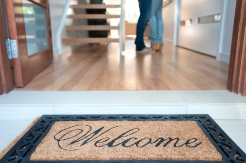 Happy young couple standing inside their new house with a welcome mat at the front door
