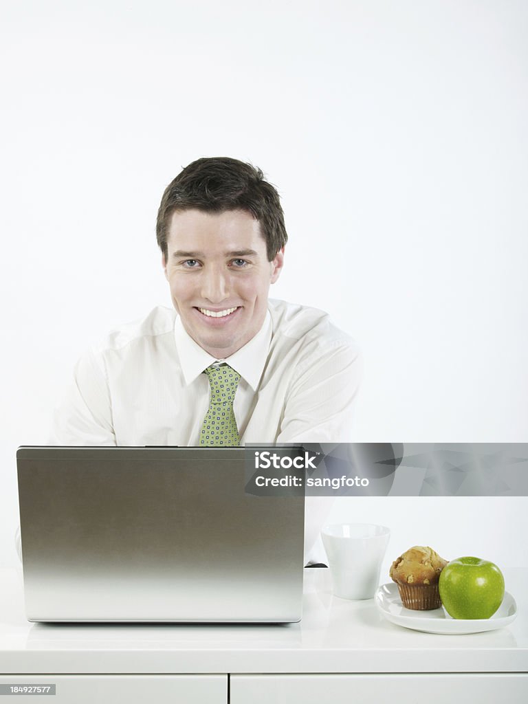 Uomo d'affari che lavorano su computer portatile sorridente con snack salutari - Foto stock royalty-free di Abbigliamento elegante