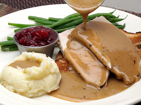 Open Face turkey sandwich with green beans, cranberry sauce and mashed potatoes with gravy pouring over potatoes and meat.