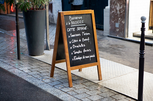 The week's specials for a butcher's shop listed on a chalkboard on a pavement in a Paris side street